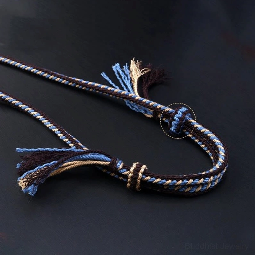 Close-up of nine-eye dzi bead necklace braided rope construction, showing blue-brown woven design with knotted fastener and decorative frayed tassel