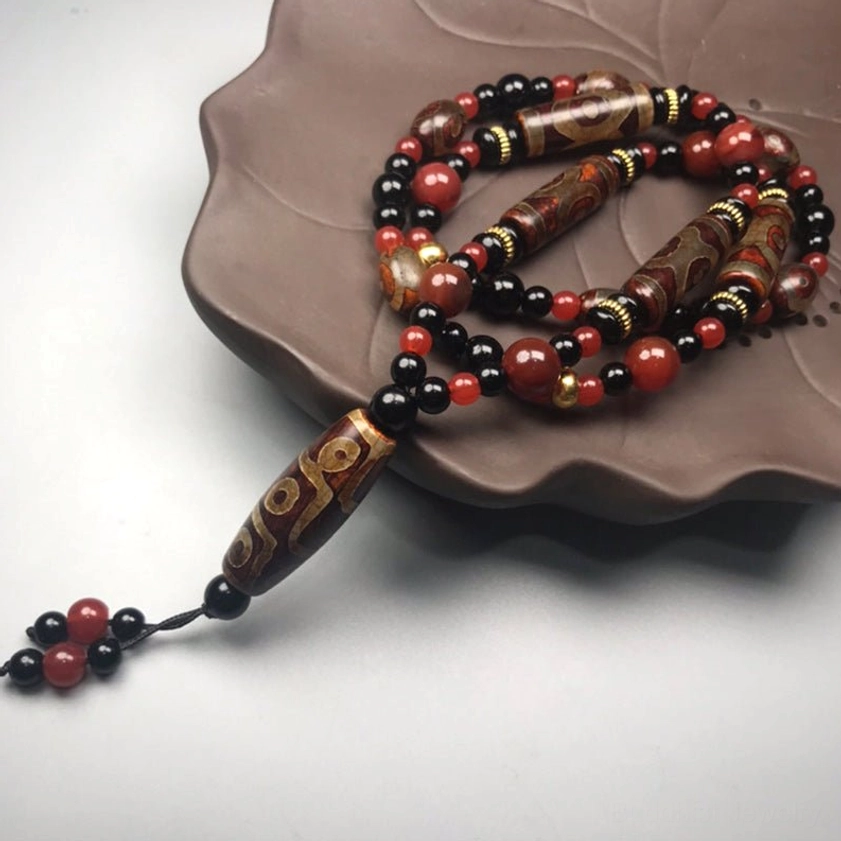 Nine-Eye Dzi Buddhist necklace 3/4 side view with red and black tassel bead end, placed on lotus-shaped ceramic holder for spiritual jewelry display