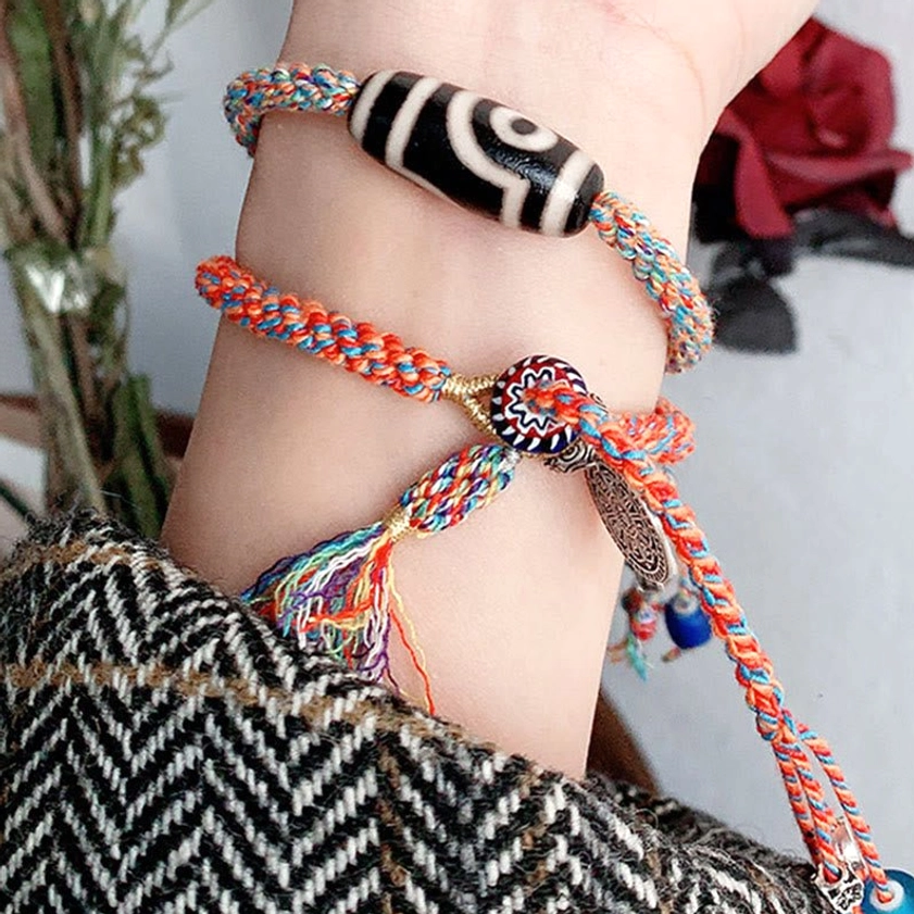 Two layered Nine-Eye Dzi Bead handmade protection bracelets stacked on wrist with black-white dzi beads, silver fasteners, and colored tassels