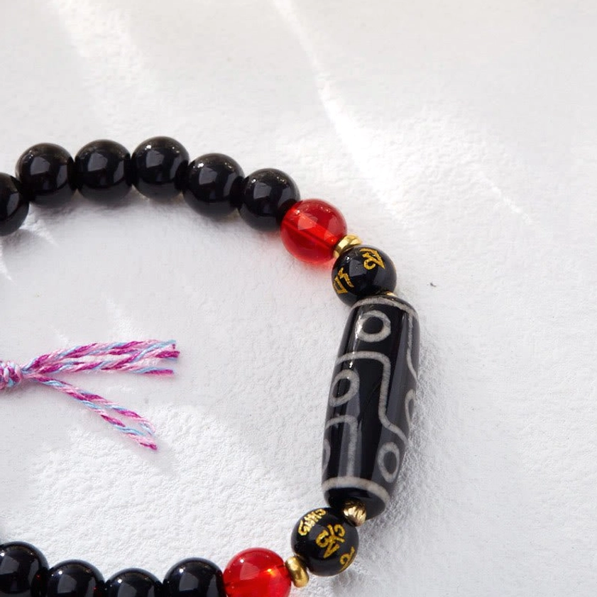 Nine-eye Dzi bead pattern macro close-up showing intricate sacred symbol details and black onyx polished stone texture