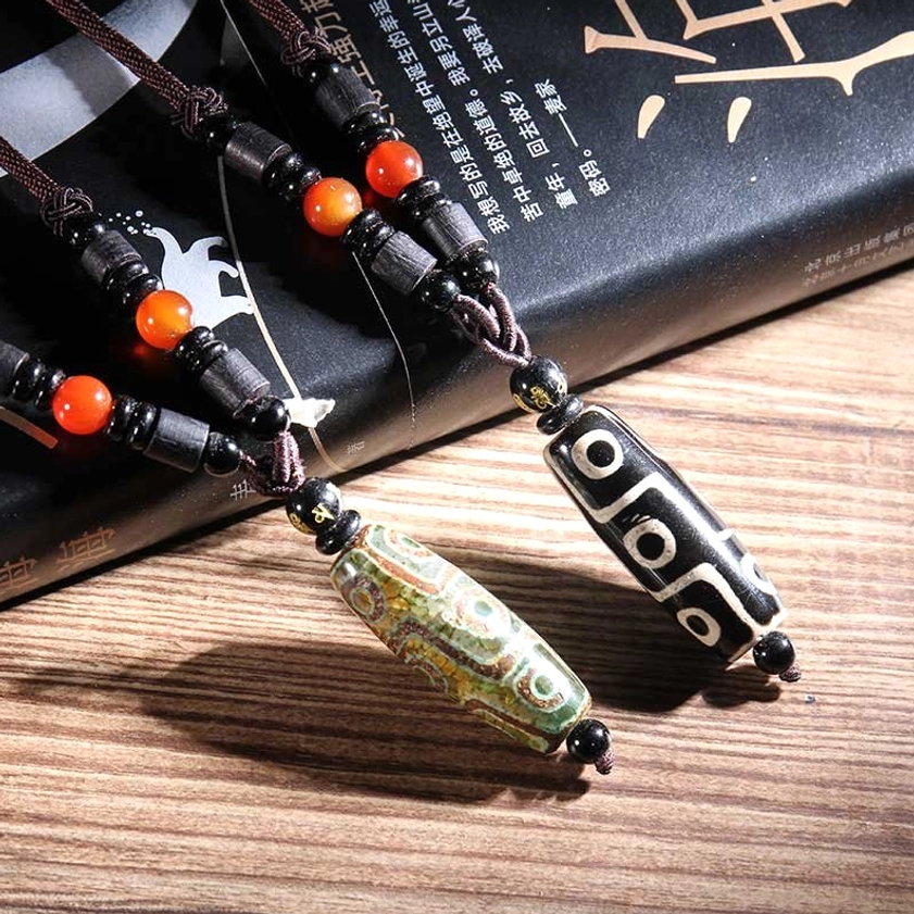 Close-up of two nine-eye dzi bead pendants showing authentic black-white and green-brown patterns with spacer beads