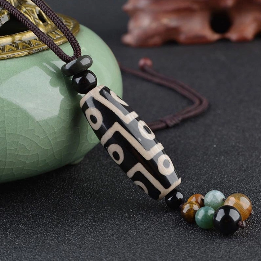 Nine-eye dzi bead Buddhist pendant with decorative beads on braided cord showcased against ceramic background