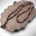 Nine-Eye Dzi Bead Red Agate Buddhist necklace flat lay on lotus ceramic tray, featuring intricately carved dzi bead with vintage patterns in reddish brown and glossy black