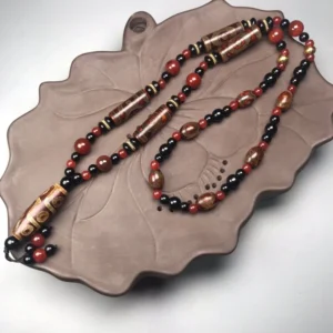 Nine-Eye Dzi Bead Red Agate Buddhist necklace flat lay on lotus ceramic tray, featuring intricately carved dzi bead with vintage patterns in reddish brown and glossy black