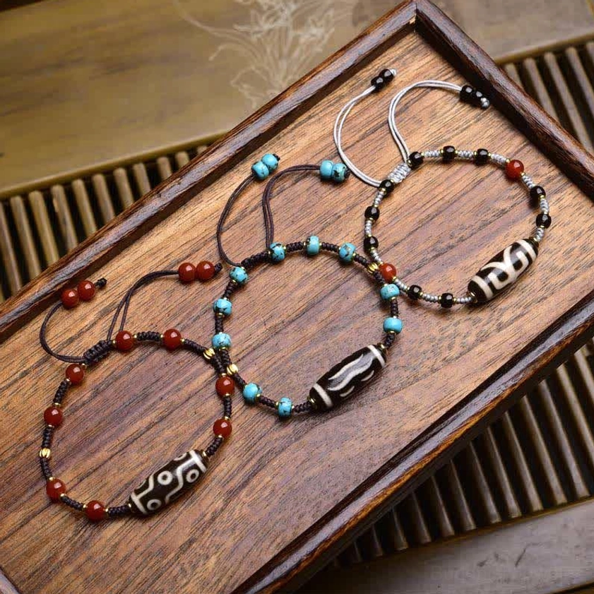 Handmade nine-eye dzi bead bracelet with south red agate and turquoise beads on adjustable woven cord, displayed on wooden surface
