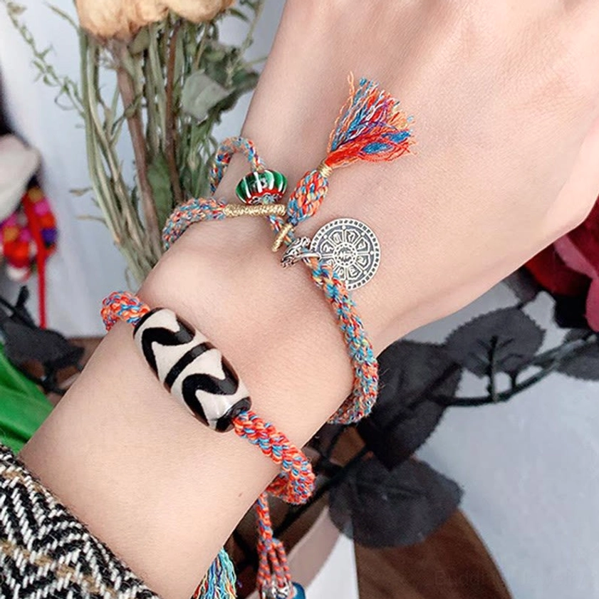 Nine-Eye Dzi Bead Om Mani Padme Hum sterling silver bracelet worn on wrist with red-orange braided rope, circular silver charm, and tassel decoration