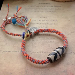 Nine-Eye Dzi Bead Sterling Silver Om Mani Padme Hum red braided protection bracelet with silver charm and colored tassels on vintage paper