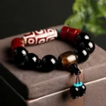 Nine-eye dzi bead black onyx bracelet displayed on dark wooden gift box with protective black beads and red agate spacers