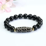 Nine-eye dzi bead black onyx Buddhist bracelet with gold spacer beads displayed on white background with pink flowers