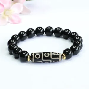 Nine-eye dzi bead black onyx Buddhist bracelet with gold spacer beads displayed on white background with pink flowers