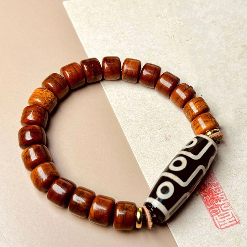 Nine-eye dzi bone bead Buddhist protection bracelet flat lay top view with red seal stamp on paper background
