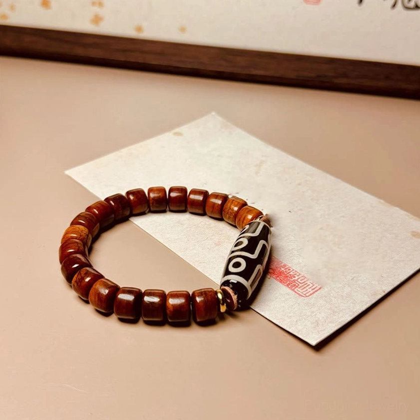 Nine-eye dzi bone bead bracelet detail shot showing deep red-brown beads and black-white dzi focal stone with red seal