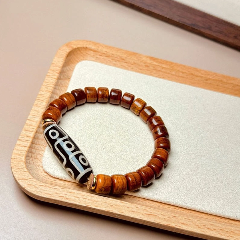 Nine-eye dzi protection bracelet overhead view on wooden tray showing warm brown bone beads and black dzi focal bead