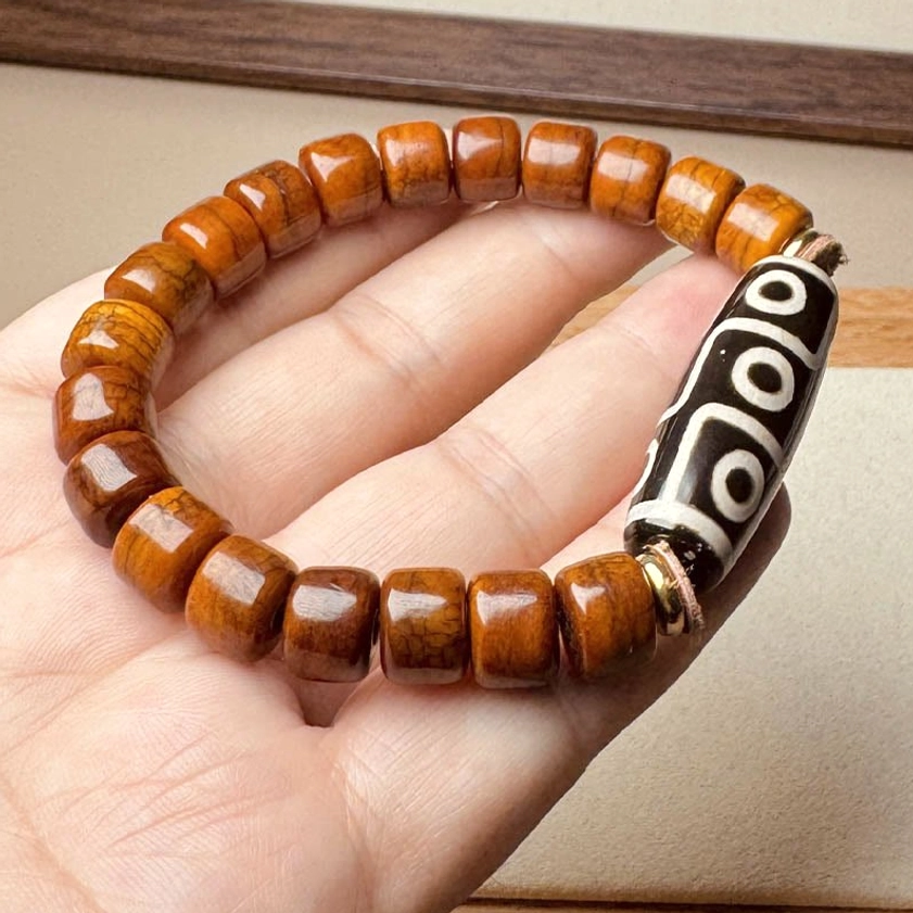 Nine-eye dzi bone bead bracelet side view in palm showing copper alloy spacer rings and bone bead detail