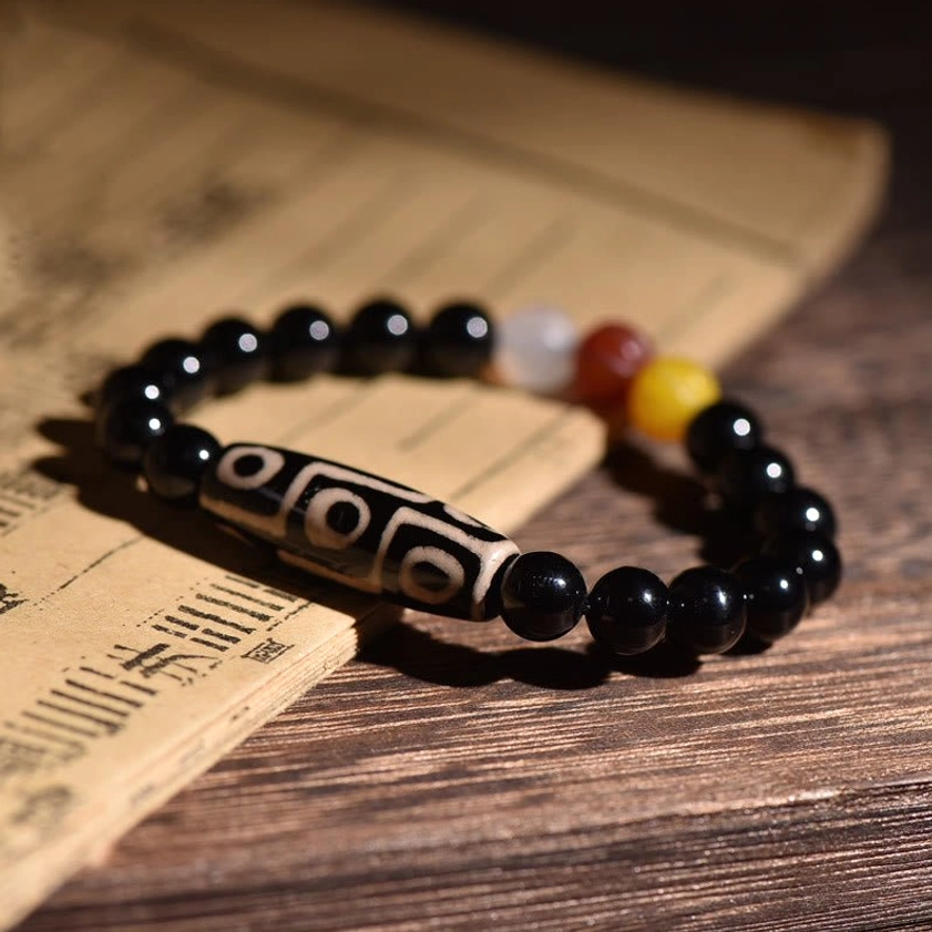 Authentic nine-eye Dzi bead bracelet displayed on antique Buddhist scroll with wooden desk, showcasing black polished beads and traditional nine-eye pattern design