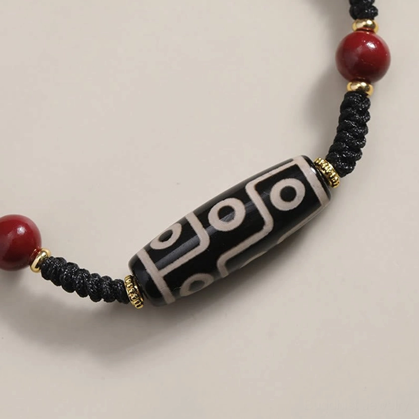 Nine-eye Dzi bead bracelet with woven black cord and distinctive nine-eye pattern on light background