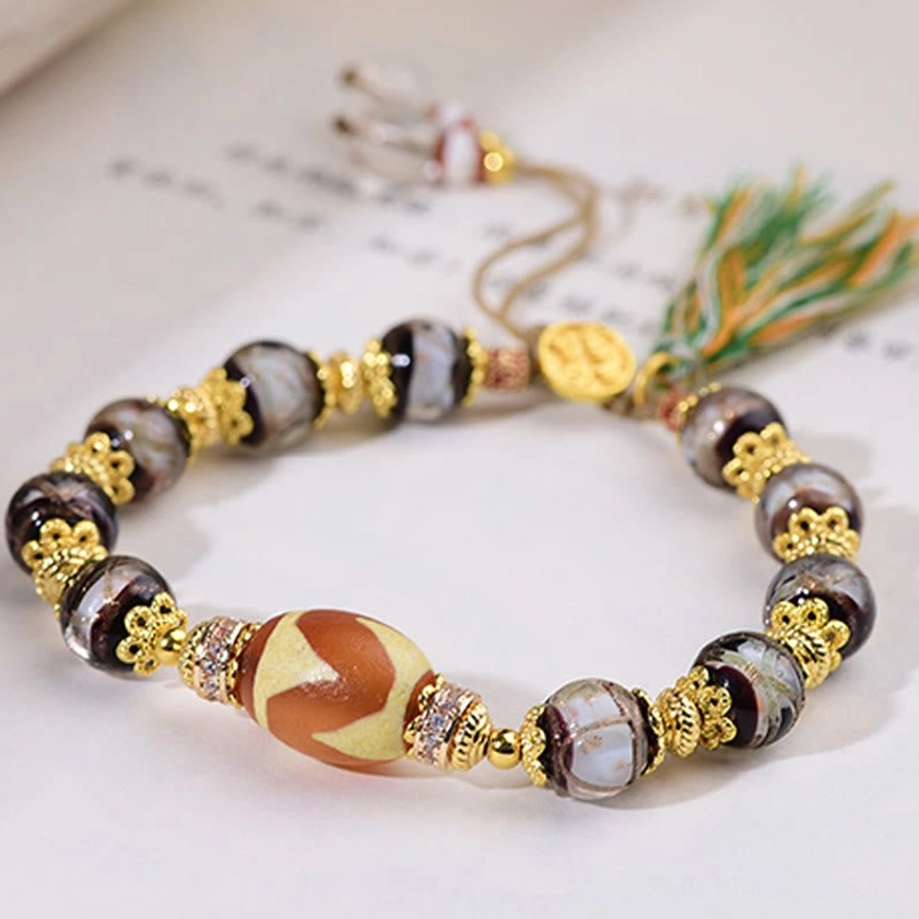 Liuli glass dzi bracelet with gold brand charm and adjustable tassel on decorative book page background