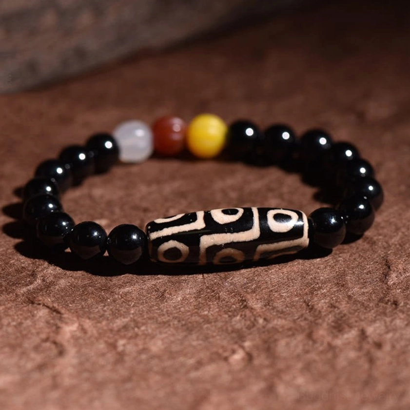 Nine-eye Dzi bead bracelet overhead flat lay view on dark background, featuring prominent central sacred Dzi bead with smooth black spacer beads in Buddhist protection design