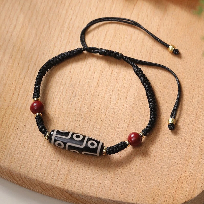 Nine-eye Dzi bead protection bracelet with red cinnabar beads and gold accents on wooden table - top view