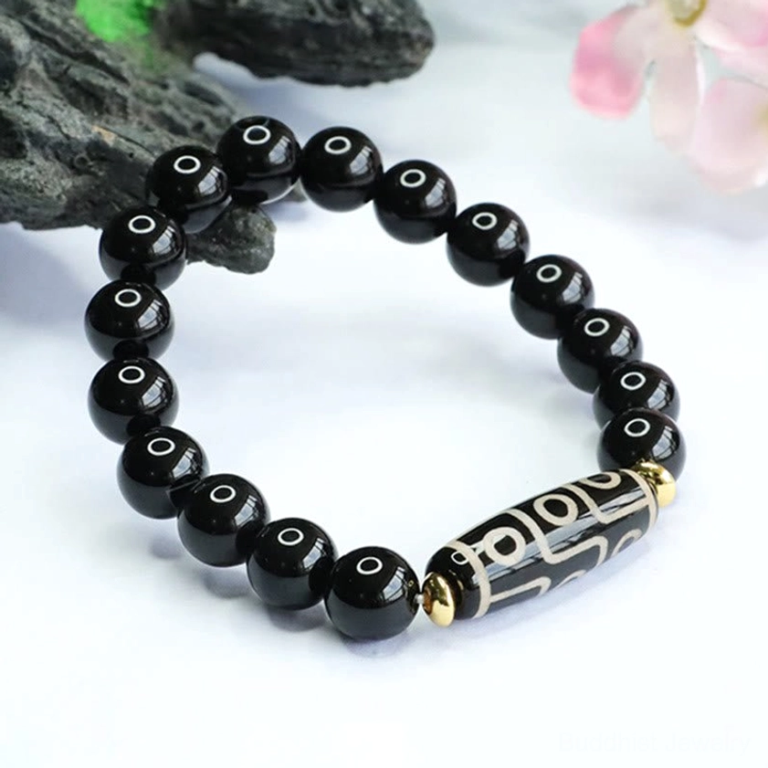Overhead flat lay of nine-eye dzi black onyx Buddhist power bracelet on dark wood with pink floral accents