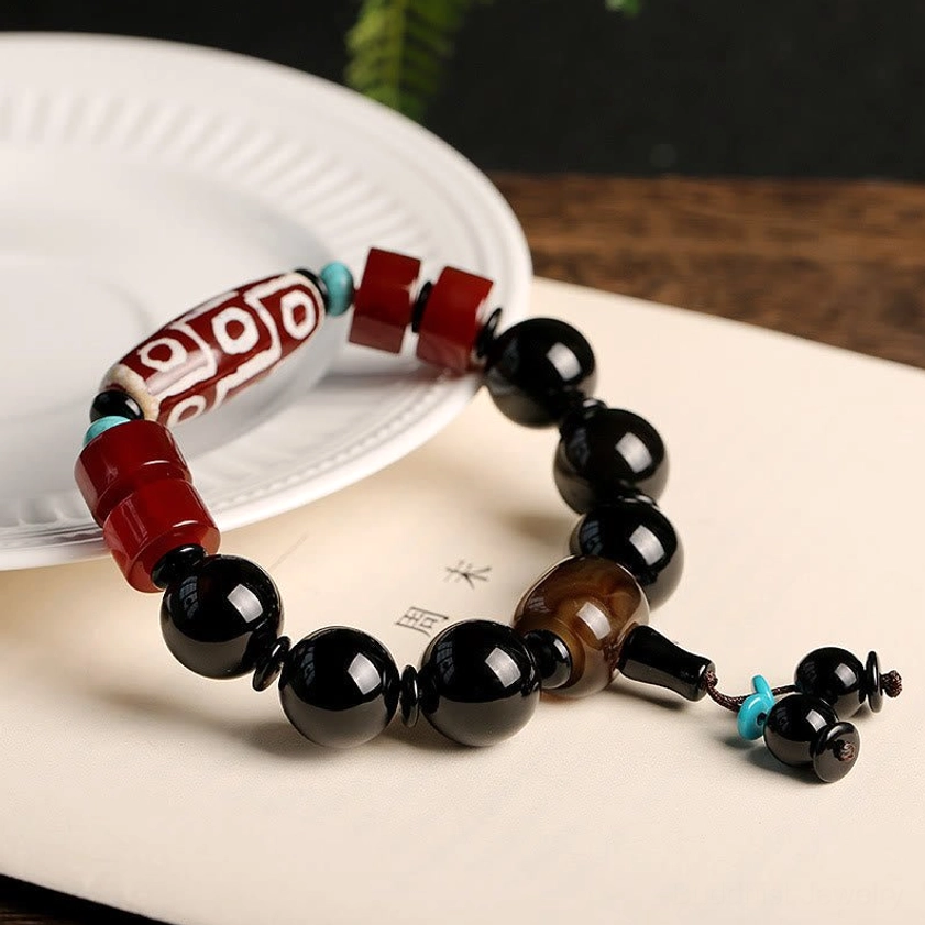 Sacred nine-eye dzi bracelet featuring black onyx and red agate spacers on minimalist white plate