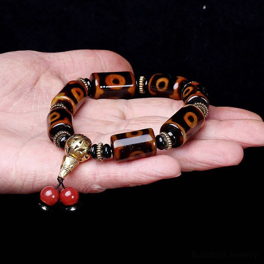 Nine-eye dzi bead bracelet held in hand against black background, showing clear bead patterns, metal guru bead, and red bead pendant