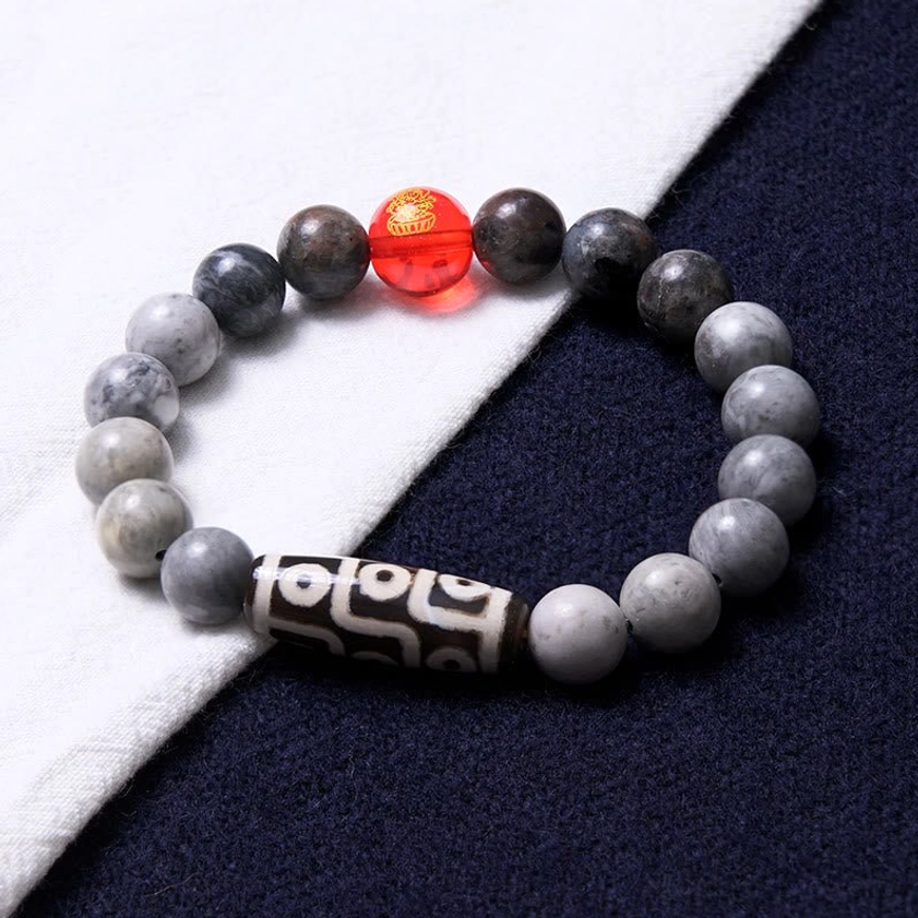 Nine-eye dzi protection bracelet flat lay on white cloth with dark blue fabric background highlighting stone bead details