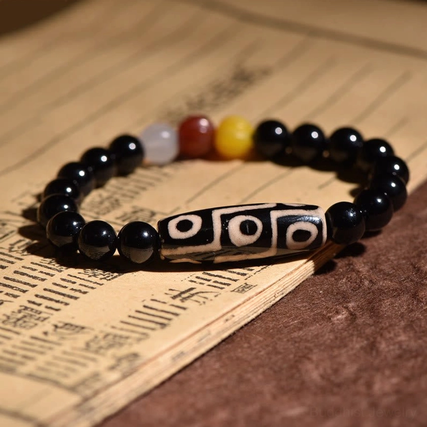 Nine-eye Dzi bead bracelet side view on traditional printed scroll background, displaying clear nine-eye sacred pattern with multicolor spacer beads