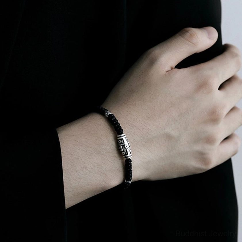 Three-quarter view of adjustable nine-eye dzi sterling silver bracelet with woven black cord and silver spacer beads
