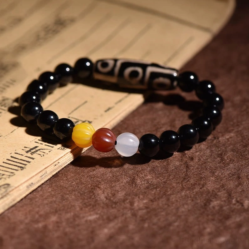 Nine-eye Dzi bead bracelet displayed on antique wooden surface with Buddhist scroll, showing traditional Dzi bead craftsmanship with reversed color spacer arrangement