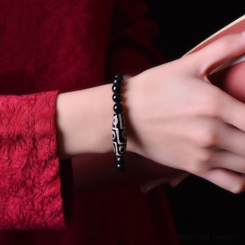 Nine-eye Dzi bead bracelet worn on wrist close-up, showing comfortable fit and visible sacred nine-eye pattern against red fabric clothing background