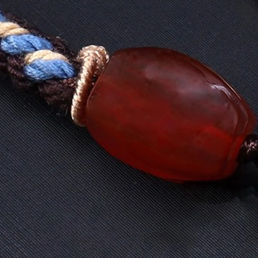 Close-up macro view of polished red agate bead spacer on nine-eye dzi necklace, showing smooth stone texture and woven rope fastener detail
