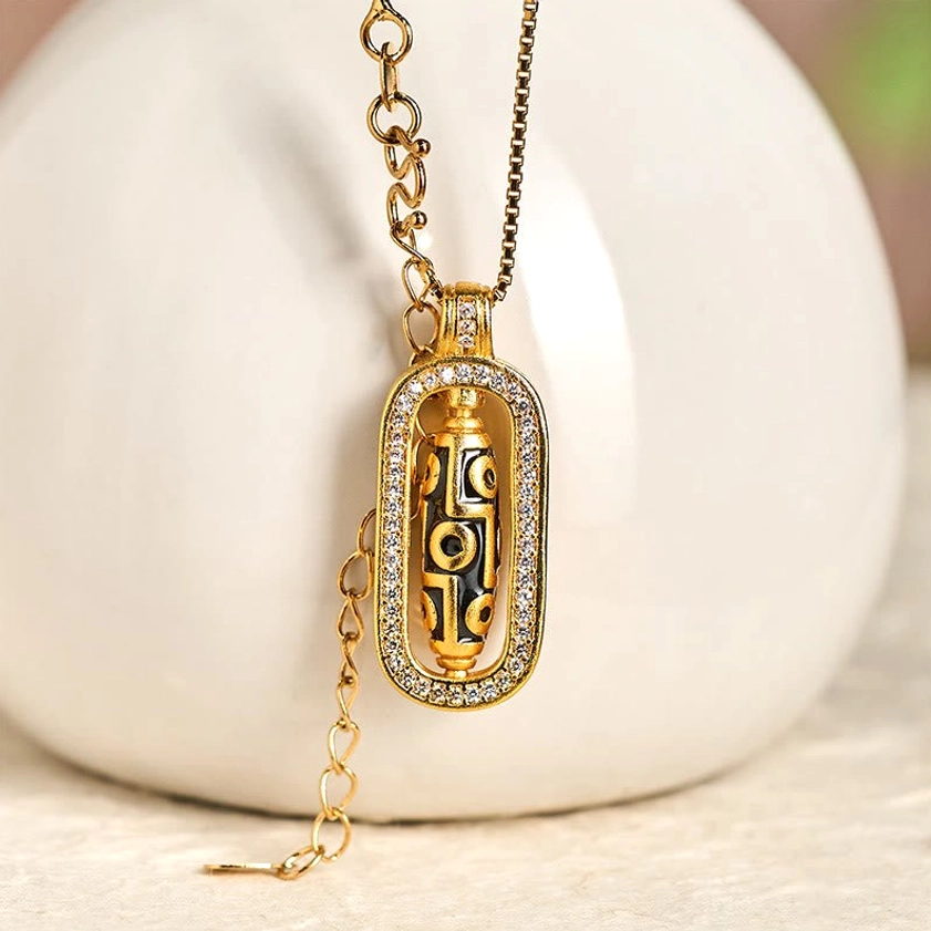 Close-up front view of gold plated dzi bead necklace with adjustable chain and diamond-trimmed pendant displayed against ceramic backdrop