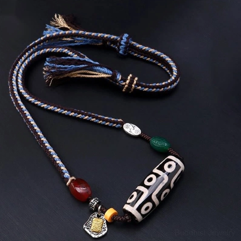 Nine-eye dzi bead necklace overhead view displaying full adjustable braided rope design with frayed tassel ends and matching agate and silver decorative elements