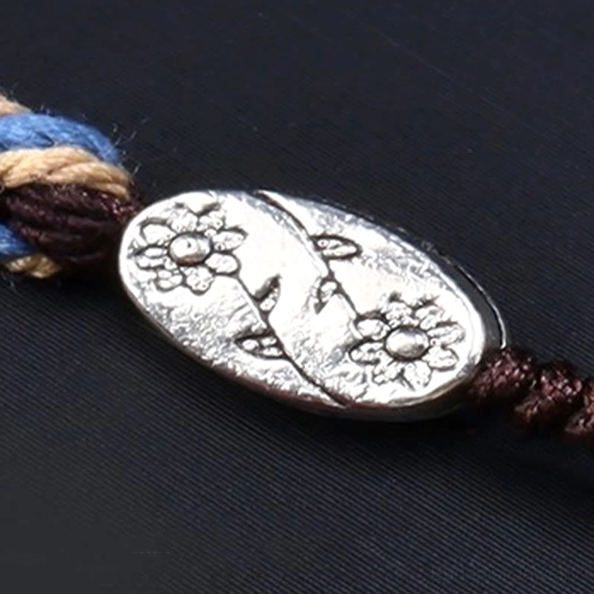 Nine-eye dzi bead necklace clasp detail showing engraved flower silver toggle with brown-blue mixed braided rope