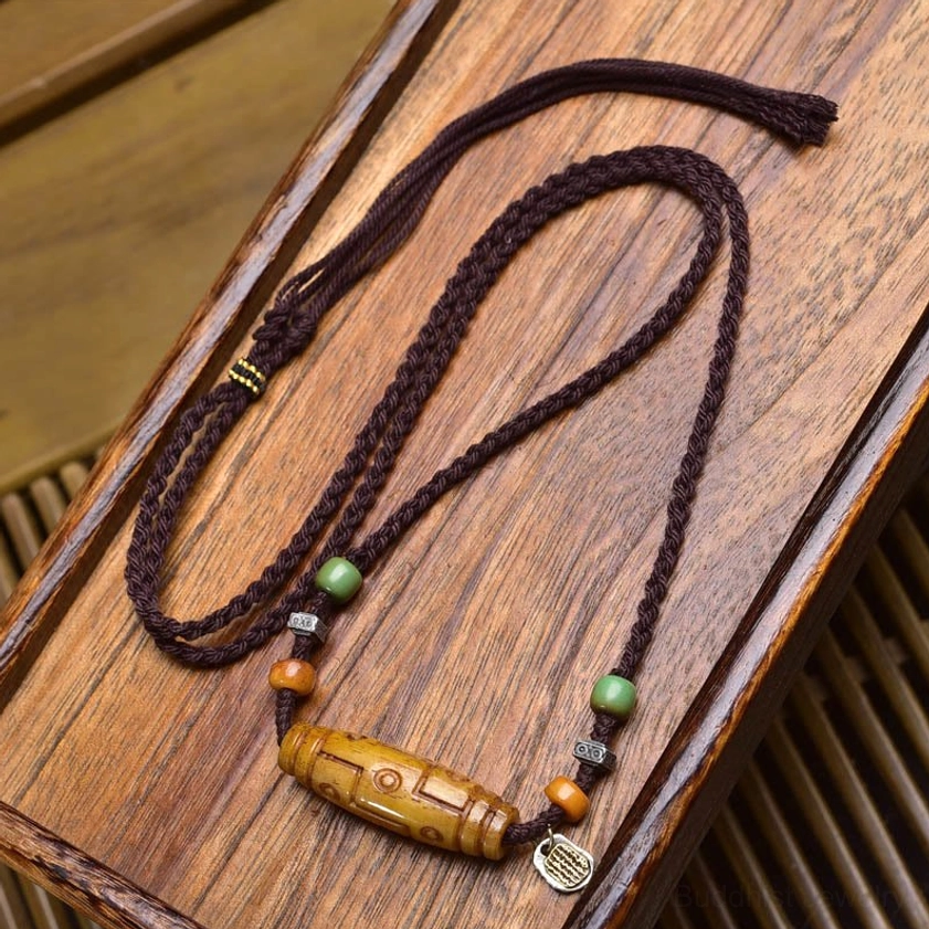 Handcrafted nine-eye dzi necklace with green and orange beads, silver engraved charm tag, and yellow dzi bead on wooden background