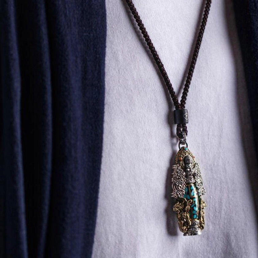 Buddhist dzi bead necklace worn on body, showing braided black cord with ornate metal and turquoise pendant for spiritual balance