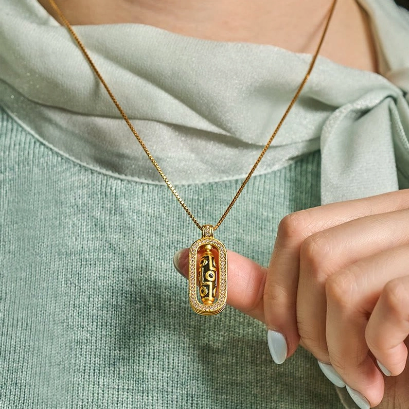 Person wearing nine-eye dzi pendant necklace at collarbone with light green blouse, showing natural fit and wearable design