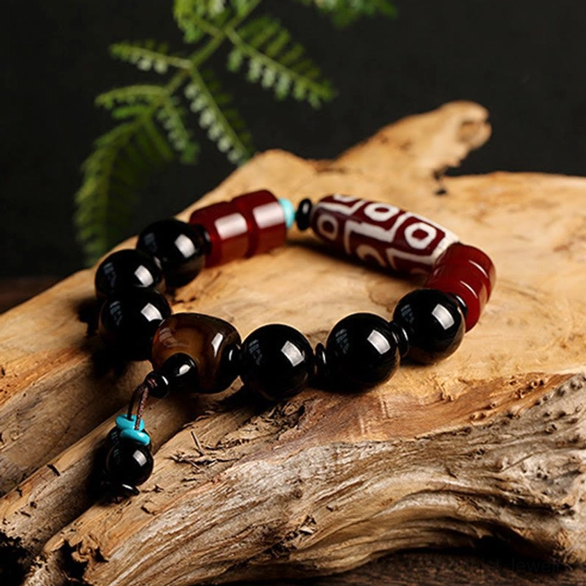 Angled view of nine-eye dzi black onyx bracelet with turquoise accents on rustic wooden surface