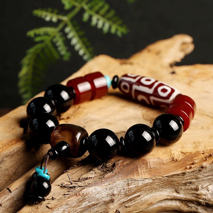 Nine-eye dzi bead bracelet with protective black onyx stones on weathered wood with natural foliage