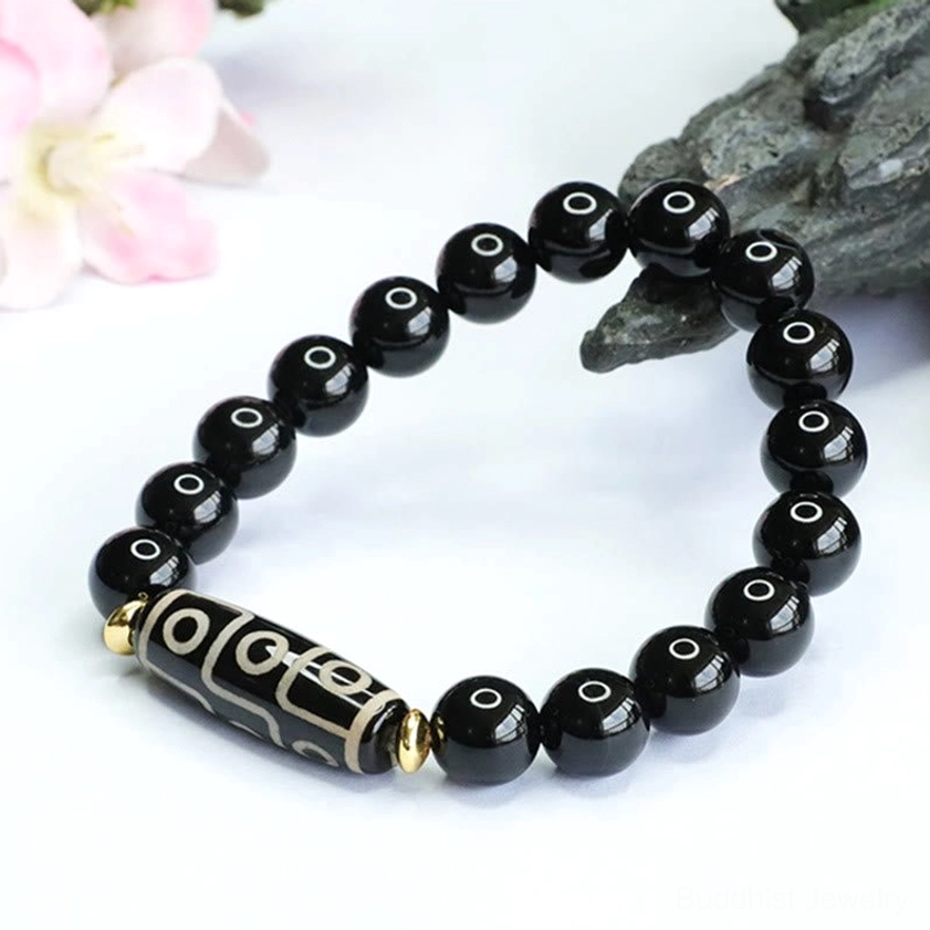Oblique top view of nine-eye dzi bead bracelet with engraved dzi charm and gold metal spacer accents on grey rock