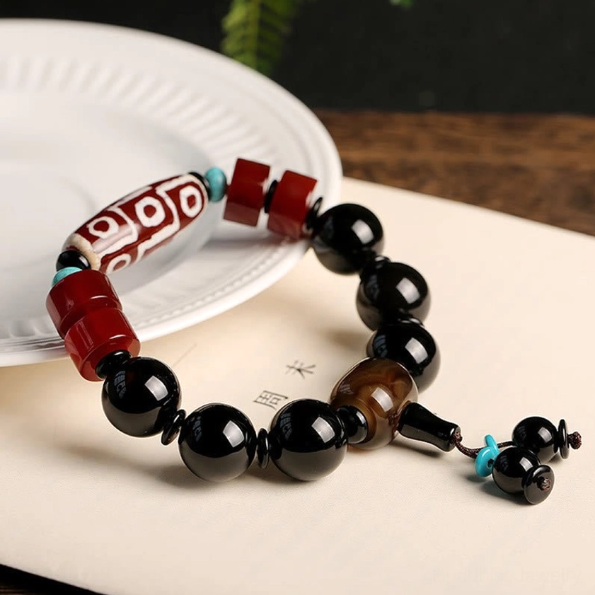 Buddhist nine-eye dzi bracelet with black onyx beads and turquoise accents arranged on white ceramic plate