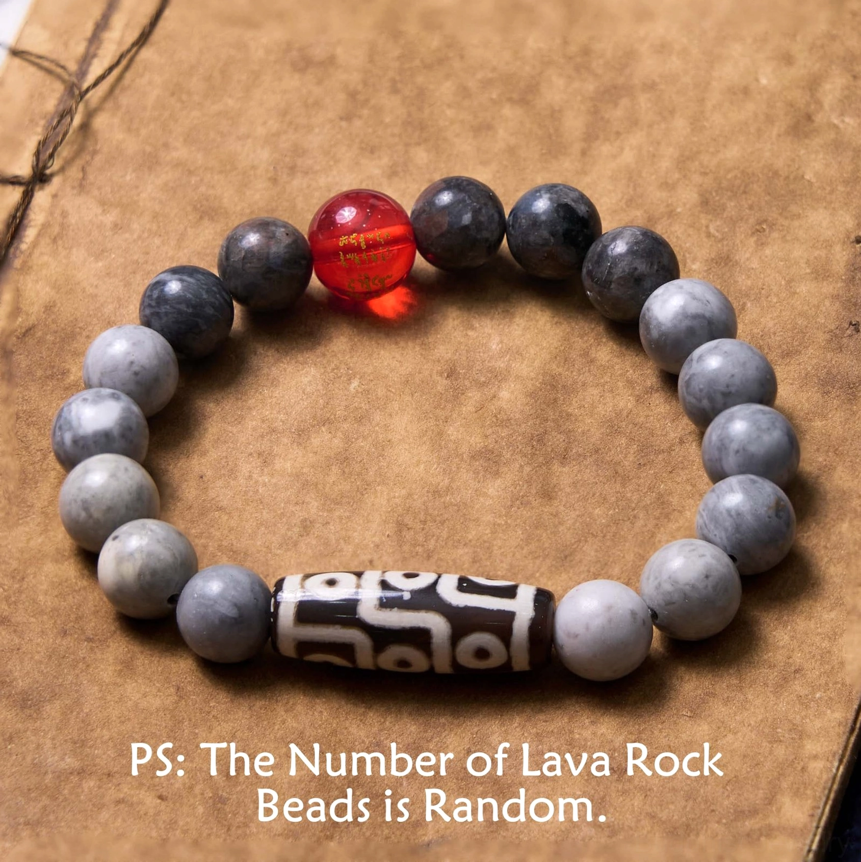 Nine-eye dzi bead picasso jasper bracelet flat lay with matte gray stone beads and red accent bead on vintage brown notebook background