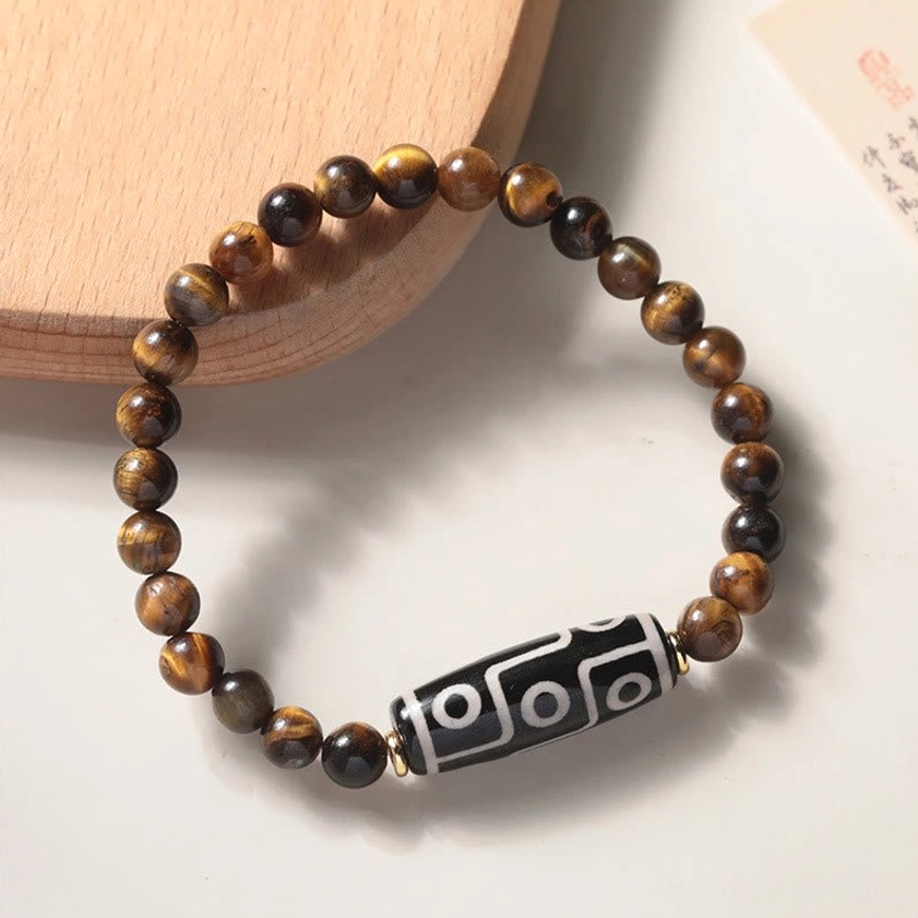 Nine-eye dzi Buddhist bracelet with tiger eye stones and gold metal spacers on curved wooden tray