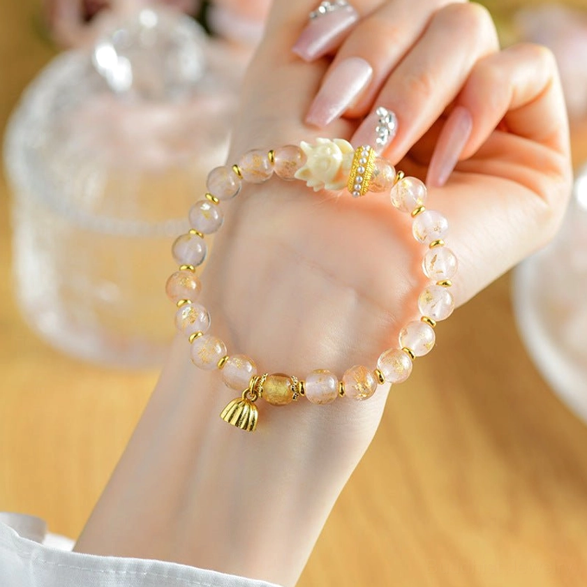 Close-up of nine-tailed fox lotus bracelet on manicured hand with pale pink liuli glass beads and gold charms, glass jar background