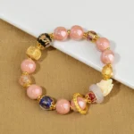 Nine-tailed fox incense ash liuli glass bead bracelet with pink beads and gold metal spacers, featuring fox charm pendant, displayed on brown desktop with white display board