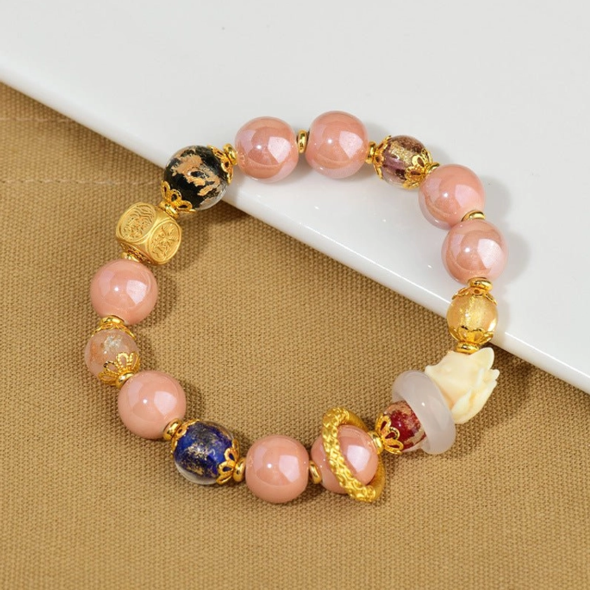 Nine-tailed fox incense ash liuli glass bead bracelet with pink beads and gold metal spacers, featuring fox charm pendant, displayed on brown desktop with white display board