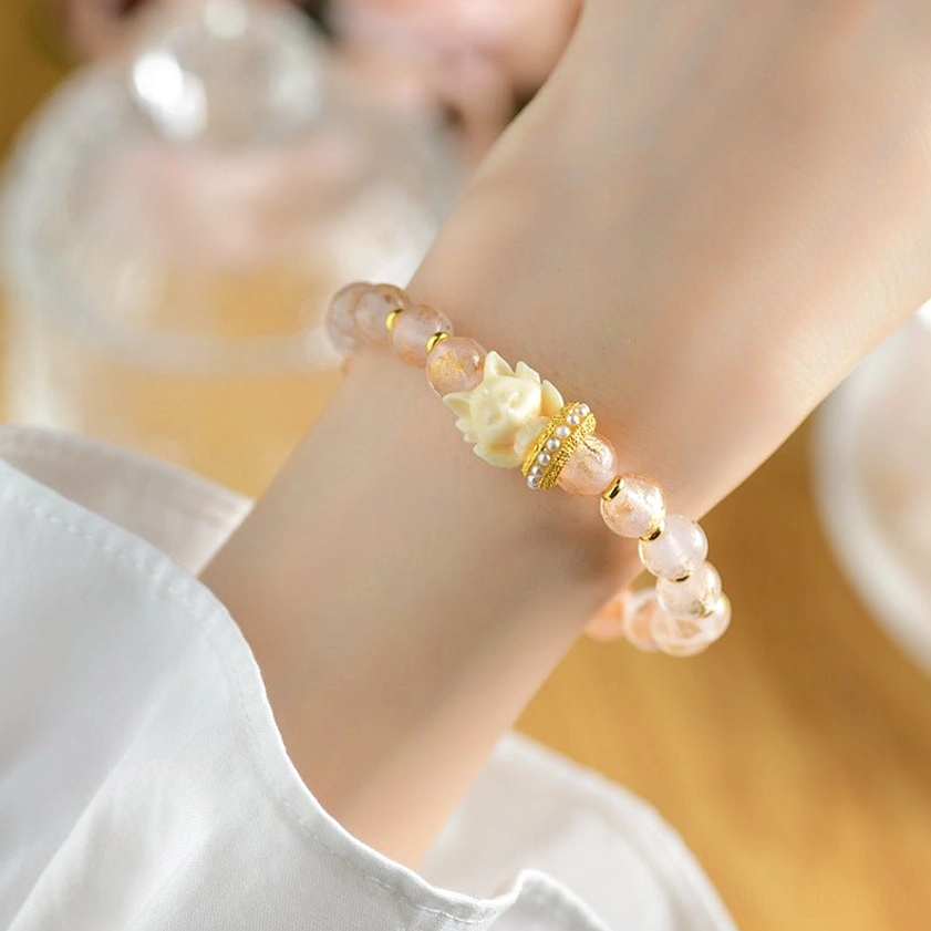Nine-tailed fox protection bracelet worn on wrist showing glitter pink beads, gold fox charm and lotus pendant, home desk setting