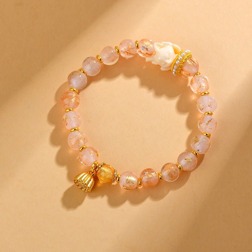 Overhead view of nine-tailed fox lotus bracelet with light pink liuli glass beads, gold hardware, and fox charm on warm tan background