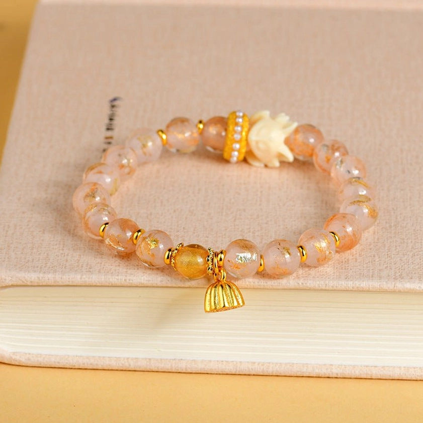 Buddhist protection bracelet with nine-tailed fox charm displayed on beige notebook, showing pink crystal liuli glass beads with gold accents